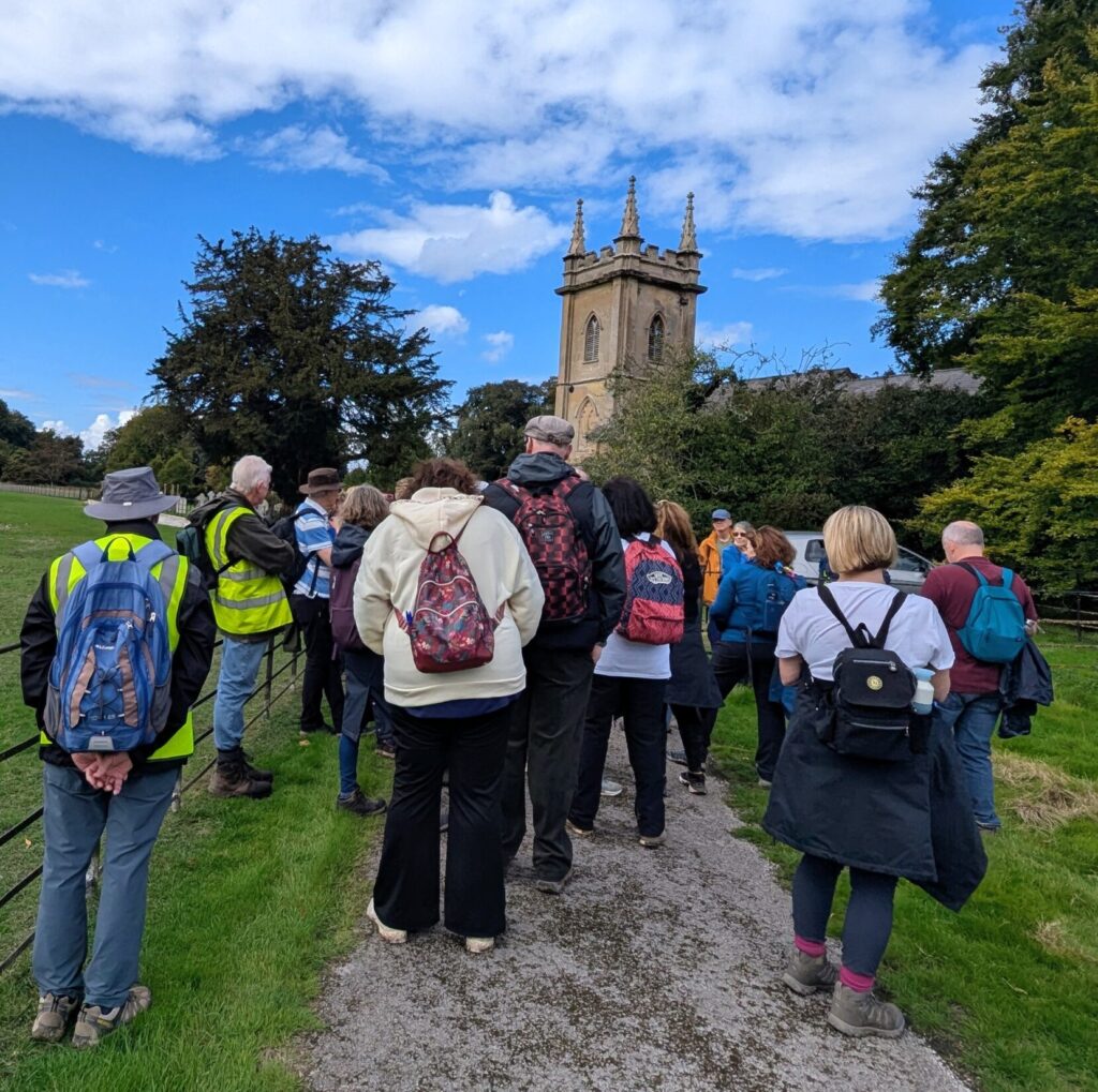 Some walkers in front of Deane Church with some mature trees and a beautiful blue sky