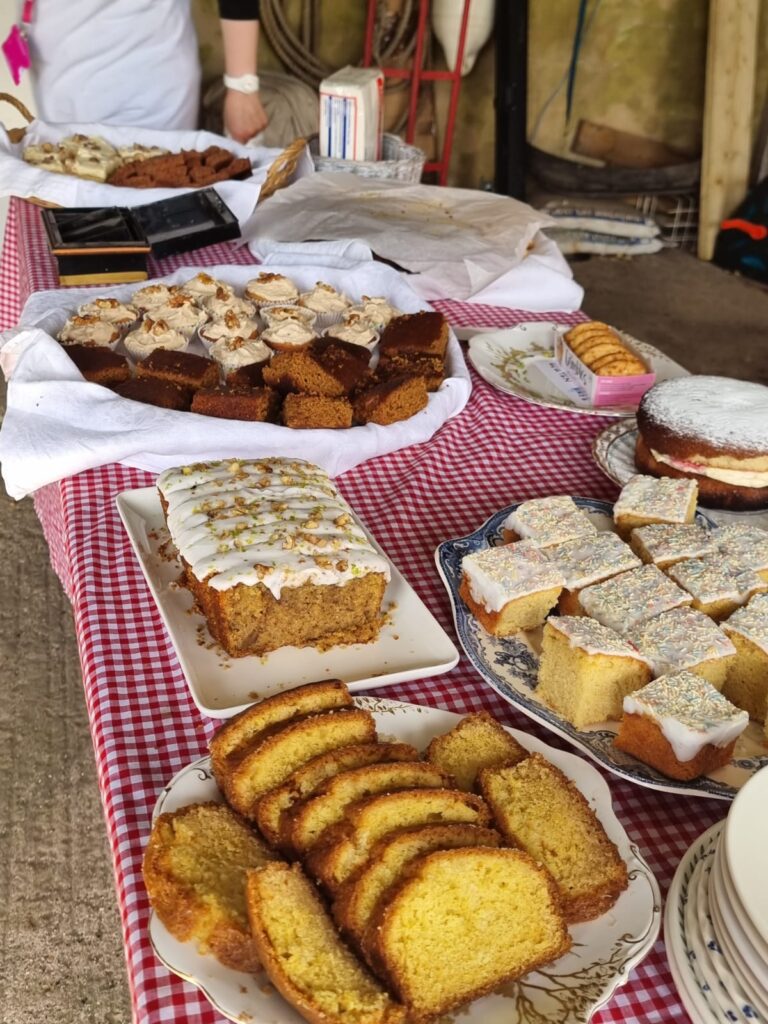 A table with a selection of delicious looking cakes on a red and white gingham tablecloth inside Quidhampton church
