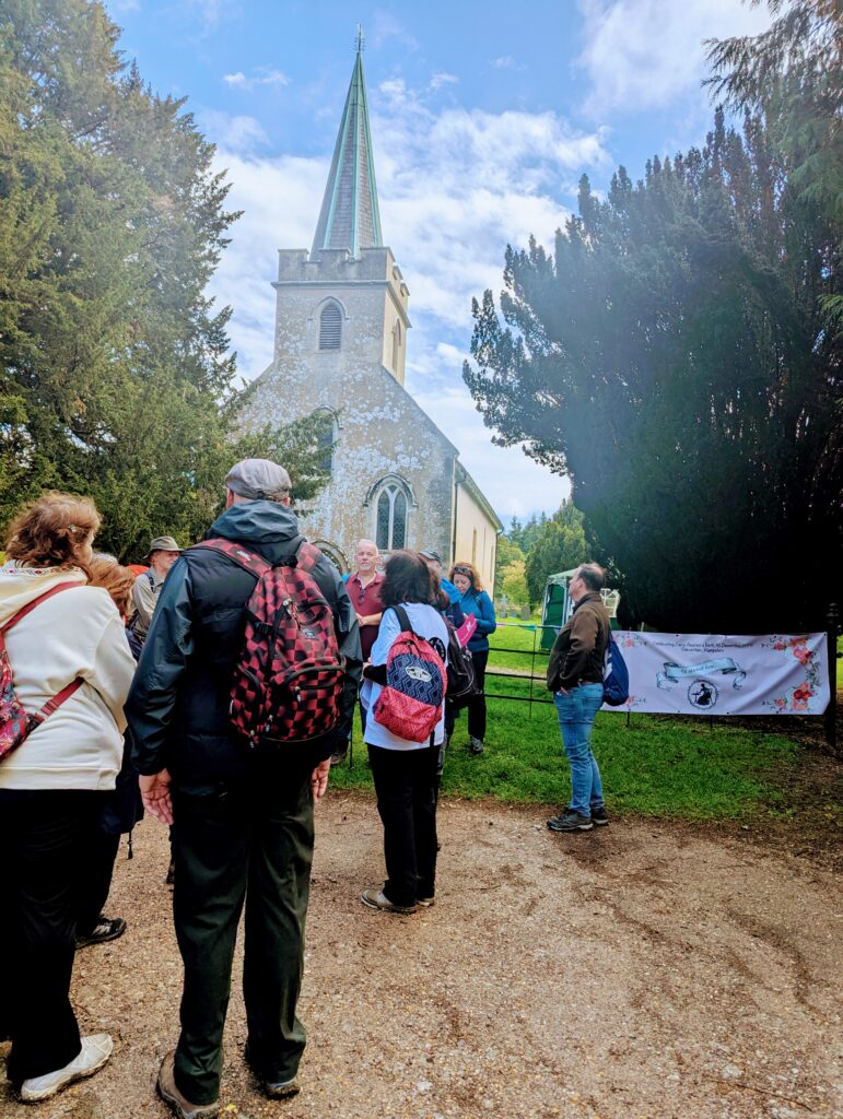 A group of walkers outside Steventon Church with the spire of the church against a beautiful blue sky